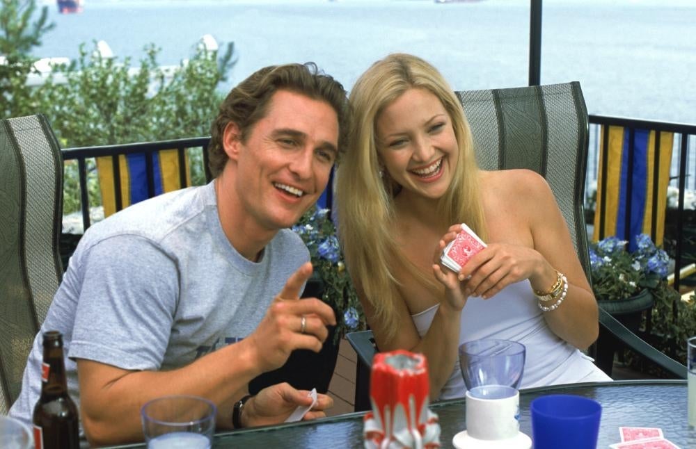 Dos personas sonrientes juegan a las cartas en una terraza. Ambiente relajado al aire libre