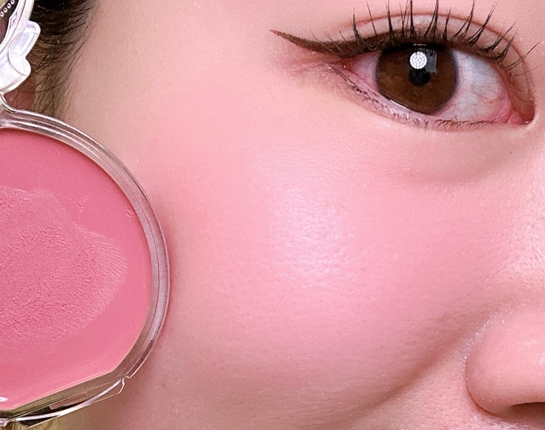 頬にピンクのチークをつけた女性の顔の一部をクローズアップ。メイクは控えめでアイラインが引かれている。