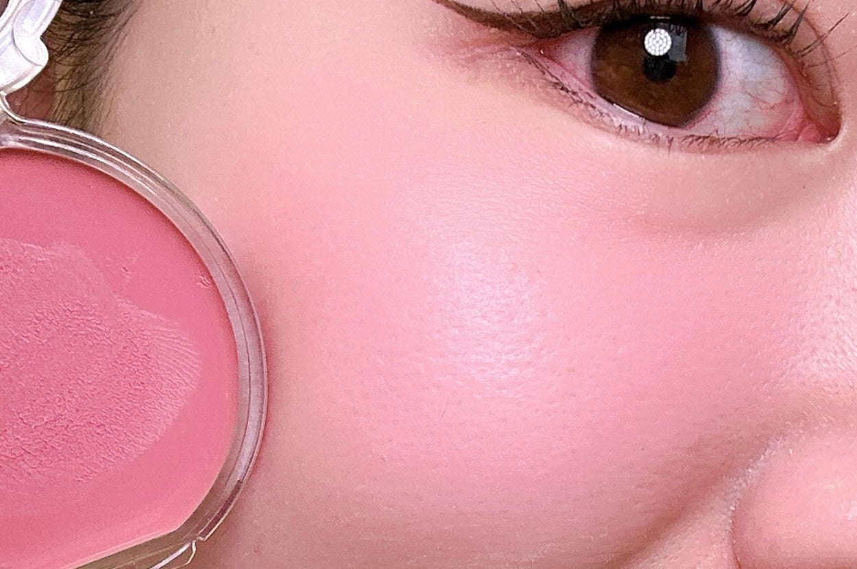 頬にピンクのチークをつけた女性の顔の一部をクローズアップ。メイクは控えめでアイラインが引かれている。