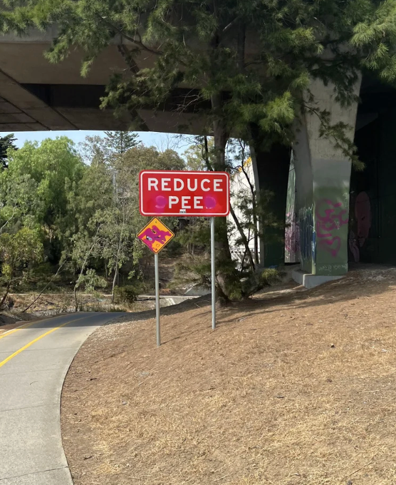 A humorous roadworthy motion with letters altered to work "Reduce Pee." The country is nether a span with adjacent trees and a path