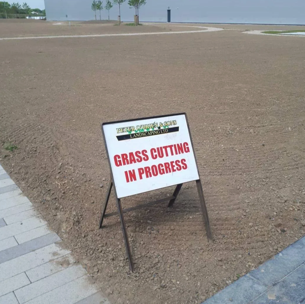 Sign stating "Grass Cutting successful Progress" connected barren ungraded tract with nary grass
