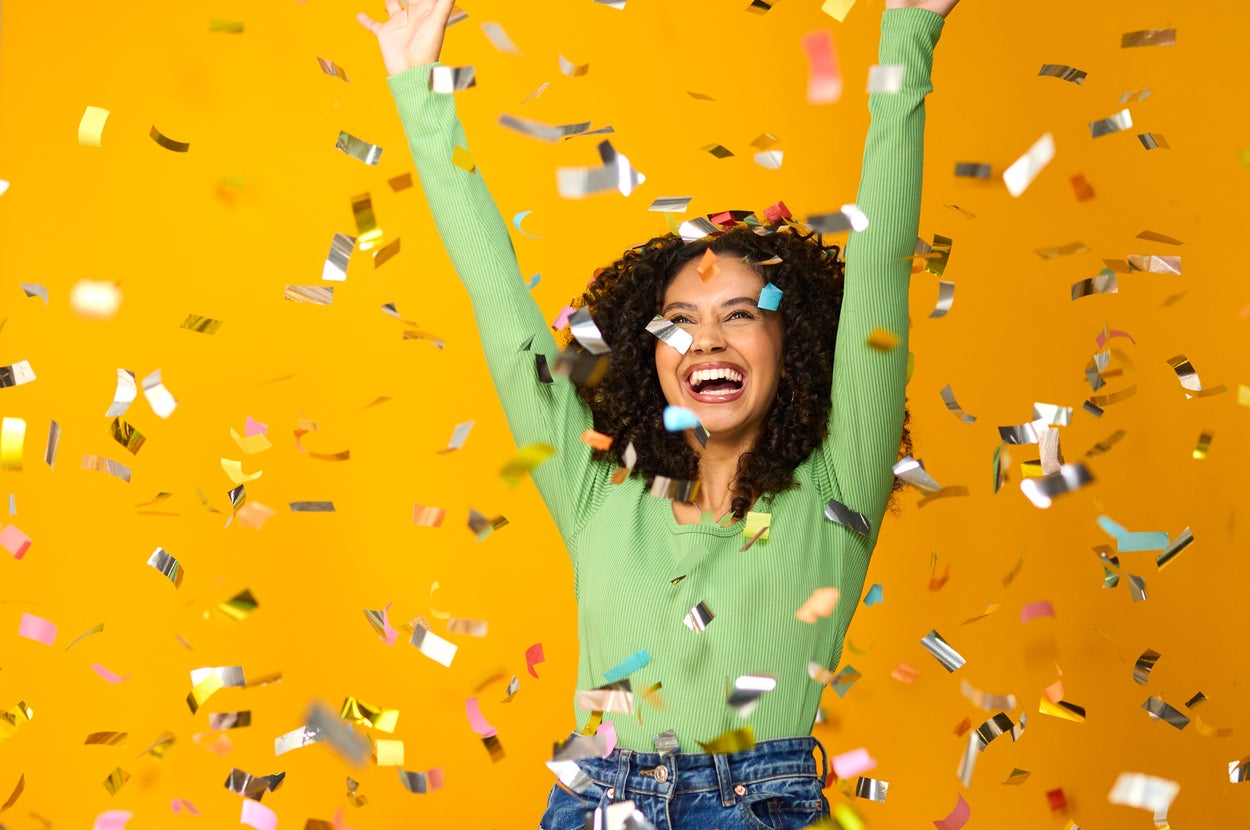 女性が楽しそうに笑いながら、両手を挙げて紙吹雪の中にいる。カジュアルな服装。