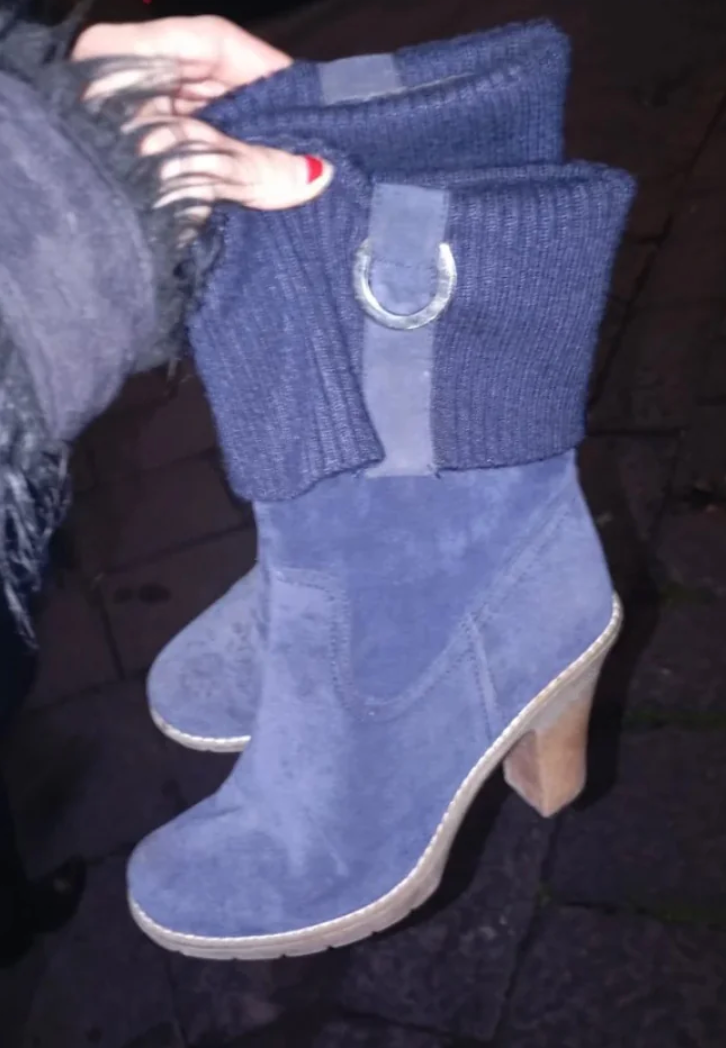 A brace of heeled ankle boots with knit cuffs and ringing details is held successful someone's hand