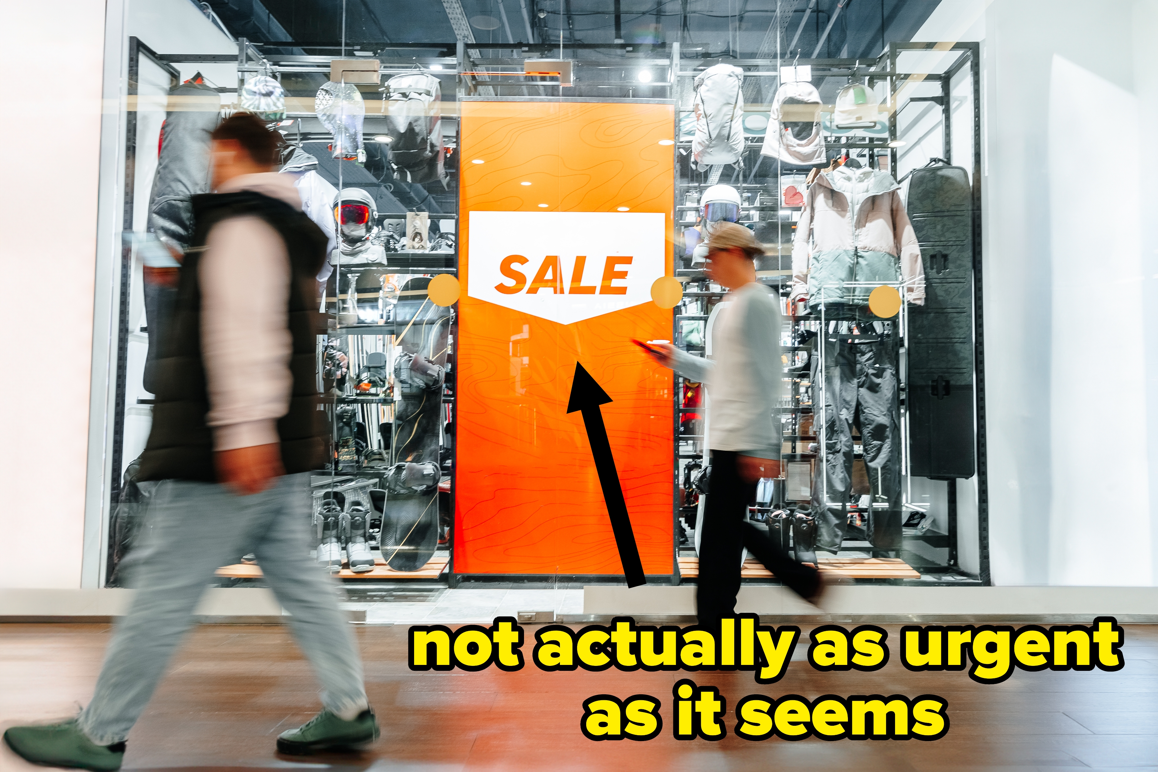 To personer går forbi et butikkvindu som viser sportsutstyr med et stort oransje "SALG" skilt