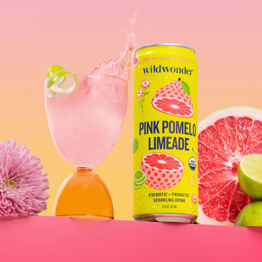 A tin  of pinkish  pomelo limeade adjacent  to a solid  with a splash, surrounded by sliced grapefruit and lime, styled for a buying  article