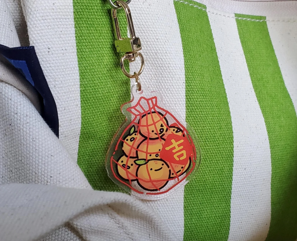 Keychain featuring cartoon oranges successful  a transparent container  attached to a striped fabric