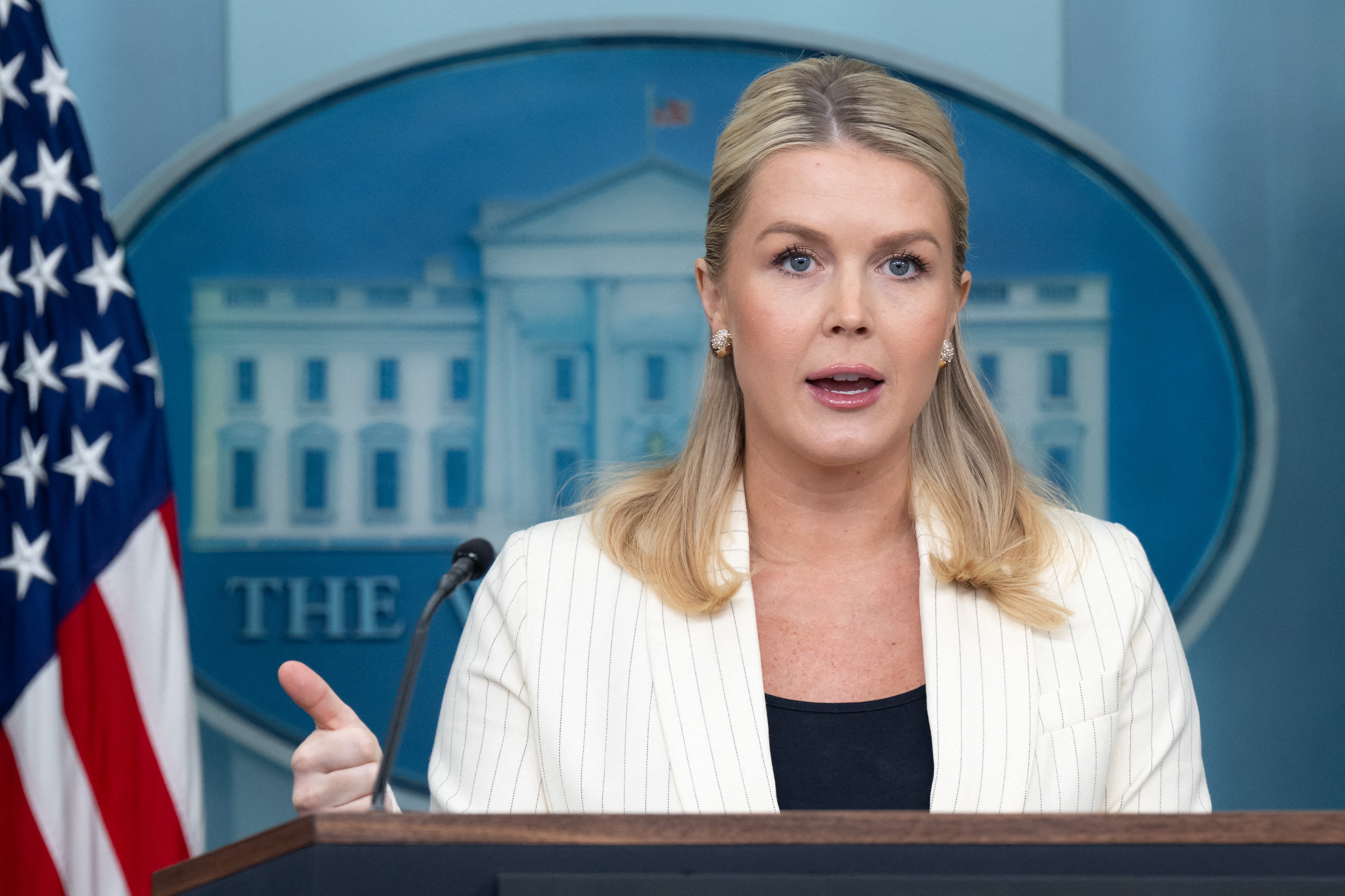 A idiosyncratic is speaking astatine a podium indoors, wearing a light-colored blazer and acheronian top, with the White House emblem disposable successful the background