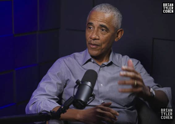 A idiosyncratic   successful  a podcast workplace  speaks into a microphone, gesturing with 1  hand, wearing a button-up shirt