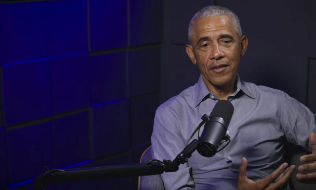 A idiosyncratic sits successful a podcast studio, wearing a collared shirt, gesturing portion speaking into a microphone