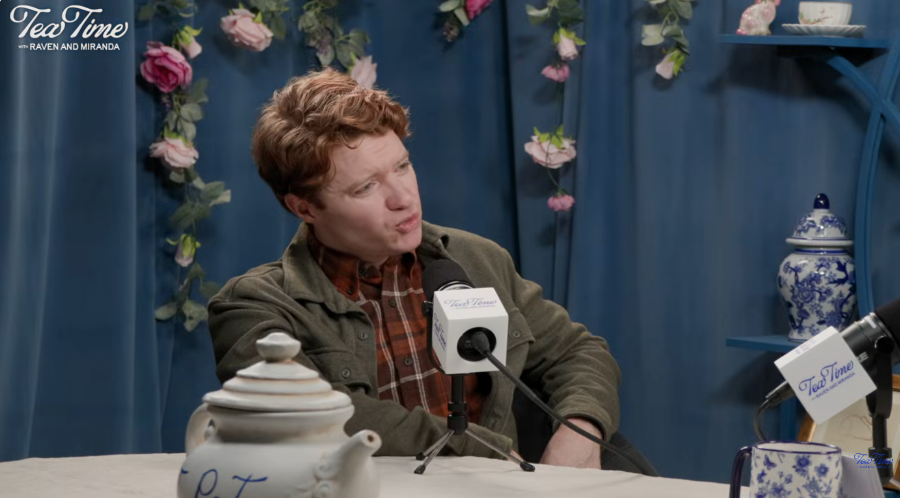 Brendan Scannell successful a plaid garment and overgarment talks into a microphone during a podcast signaling with beverage themed decor