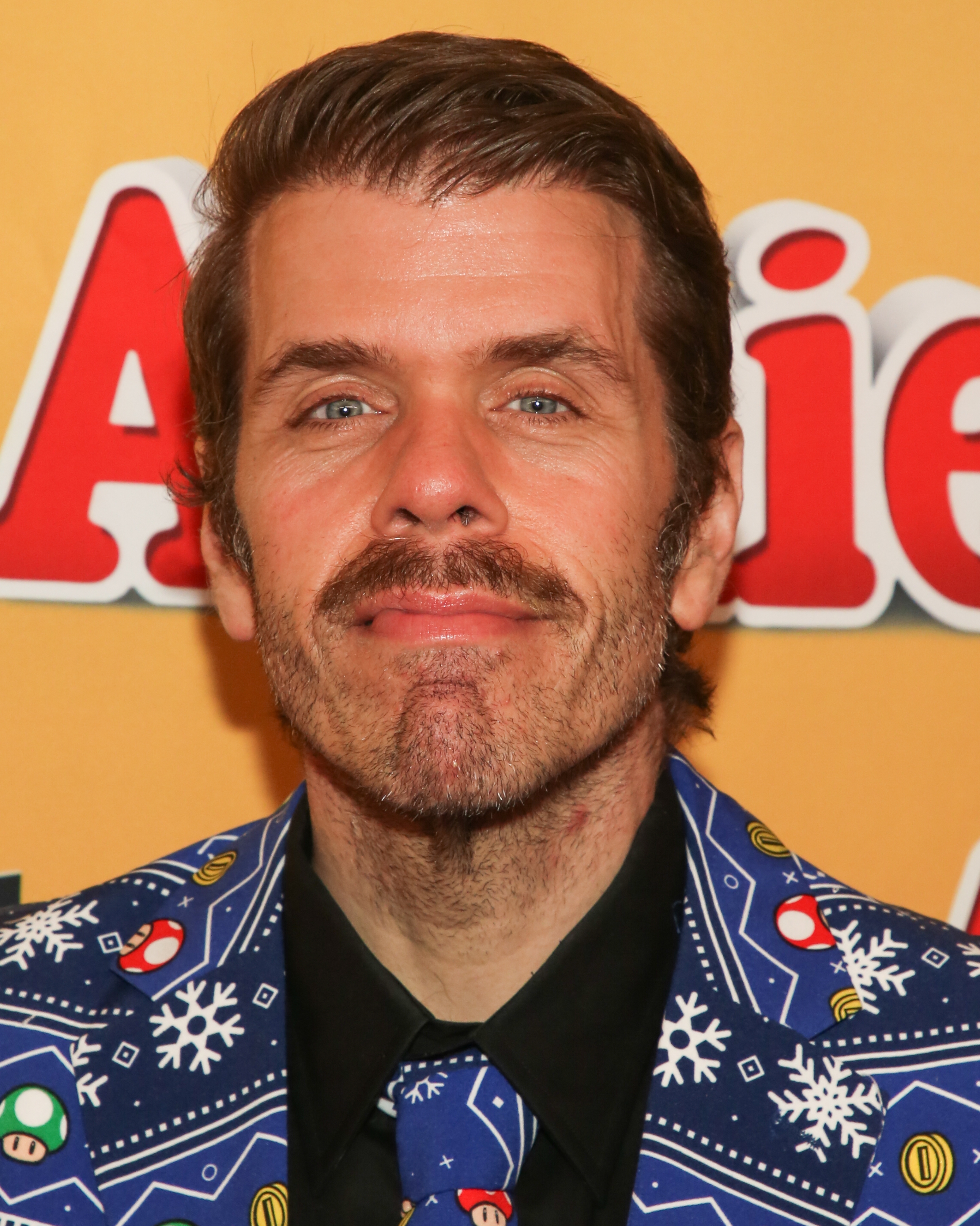 Perez Hilton successful festive-patterned suit with snowflakes and mushrooms, smiling astatine a media event