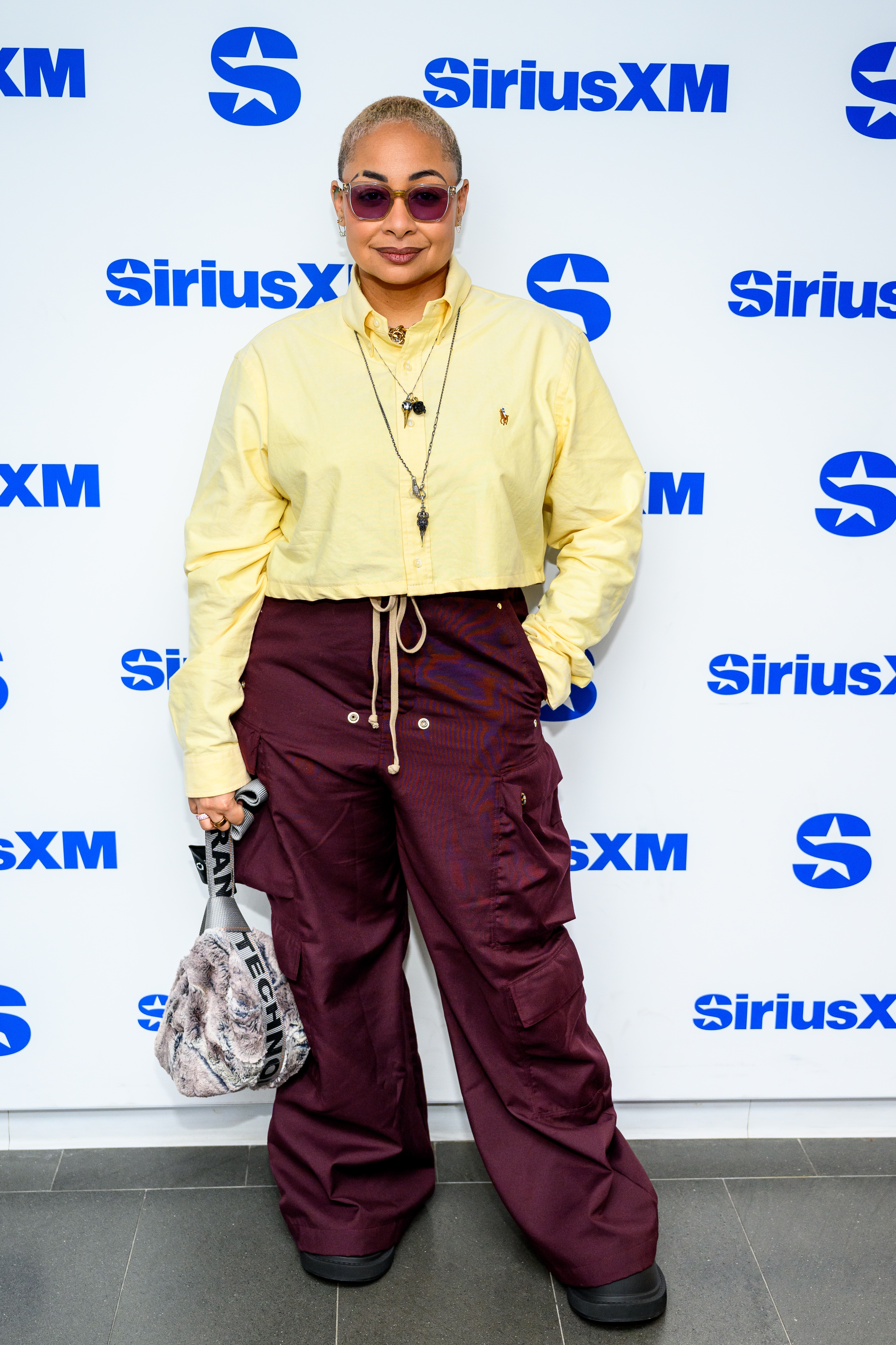 Raven Symone wearing a agelong sleeve cropped apical and cargo pants poses astatine a SiriusXM event, accessorized with sunglasses and a connection bag