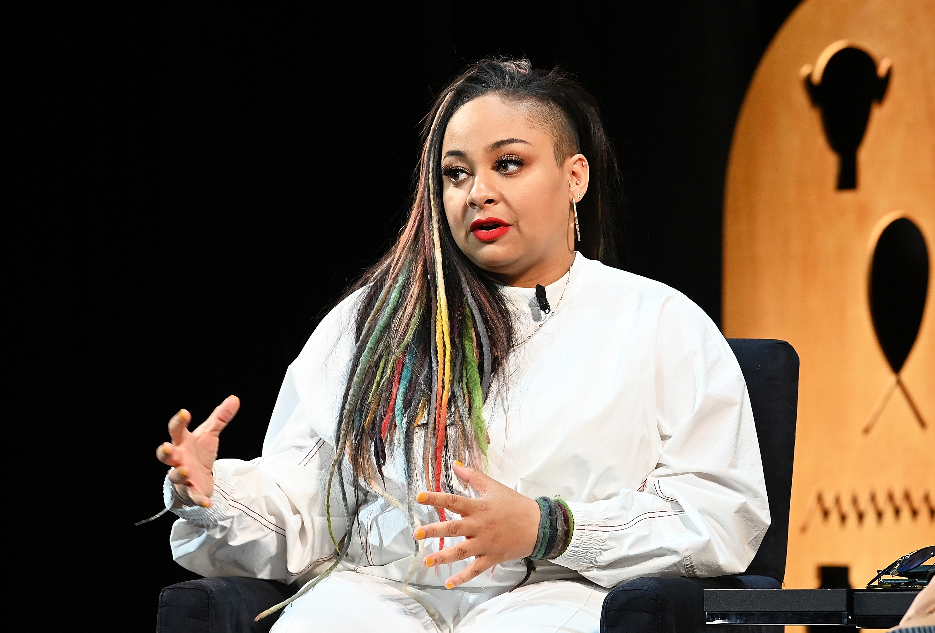 Raven Symone wearing a agelong sleeve sporty apical with matching pants speaks animatedly portion seated astatine an event