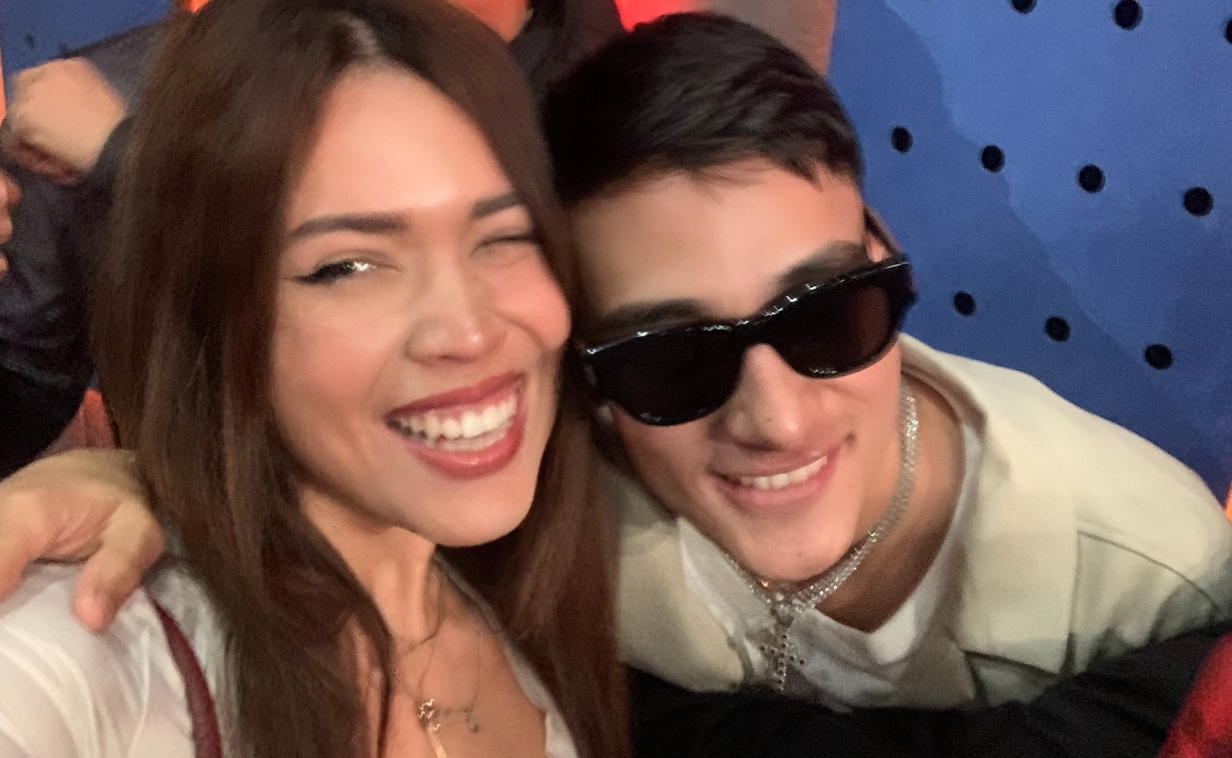 No sé quiénes son, pero hay una persona sonriendo y otra con gafas de sol y collares. Están abrazados y parecen estar en un evento casual