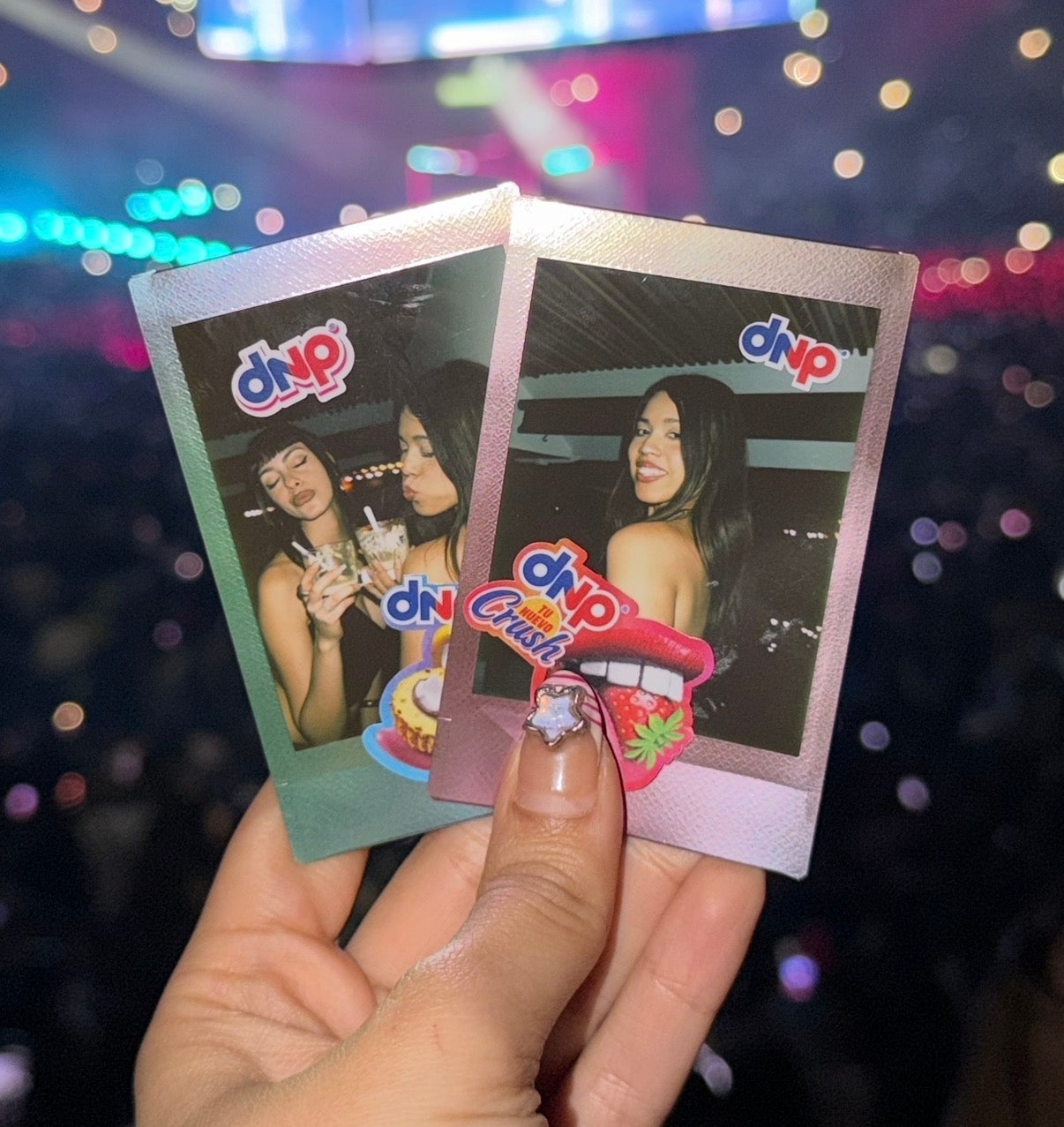 Primer plano de dos fotos instantáneas sostenidas por una mano en un concierto con luces brillantes de fondo