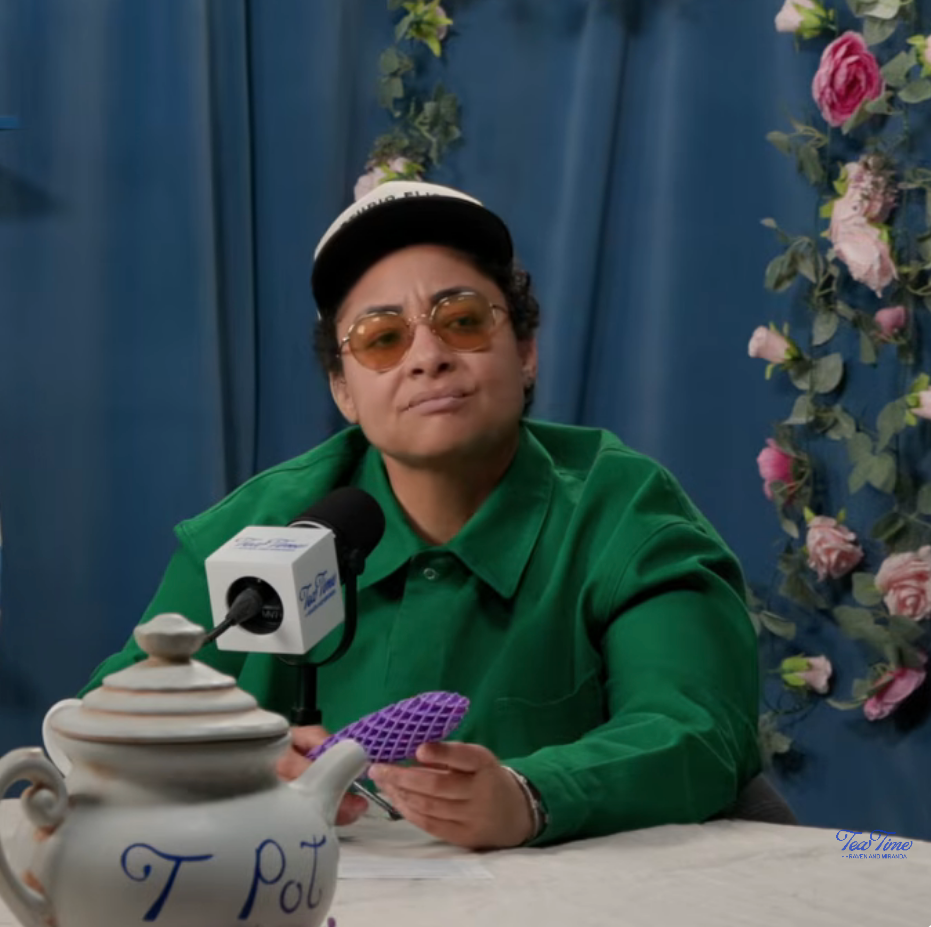 Raven Symone successful a casual mounting wearing sunglasses, a cap, and a fastener up shirt, holding an point during a podcast interview