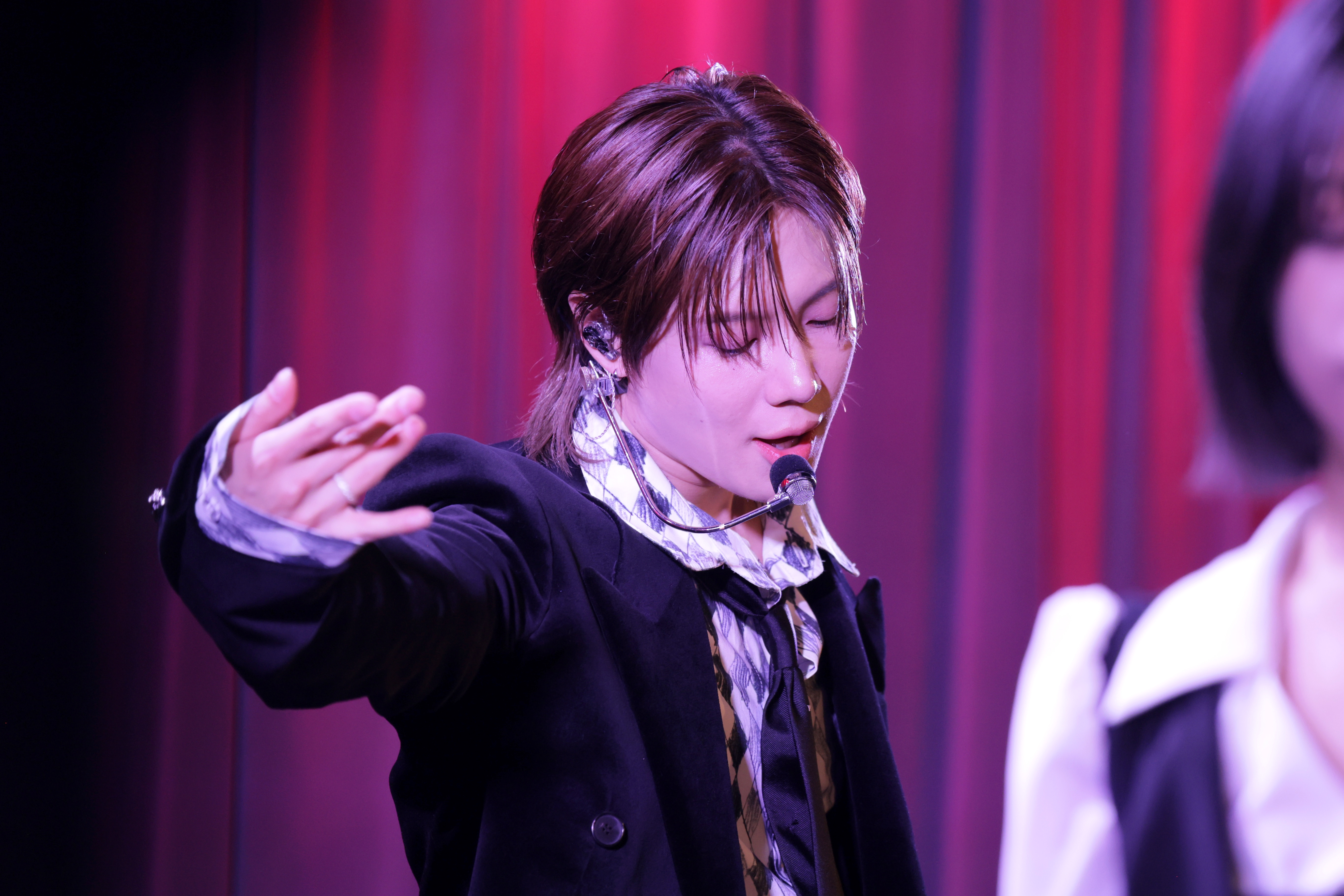 Utøver på scenen iført dress med rutete skjorte og slips, synger inn i en hodesettmikrofon med en dramatisk håndbevegelse