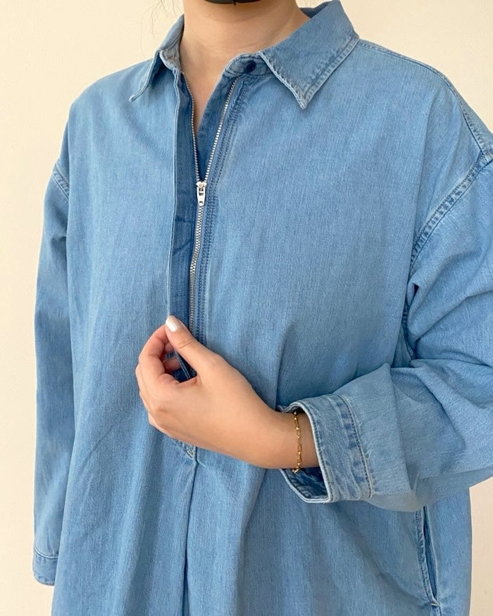 無印良品の「婦人 カポック混 ライトデニム 長袖ワンピース」女性がデニムシャツを着ている。左手でシャツの前を軽く持ち、袖を少しロールアップしている。