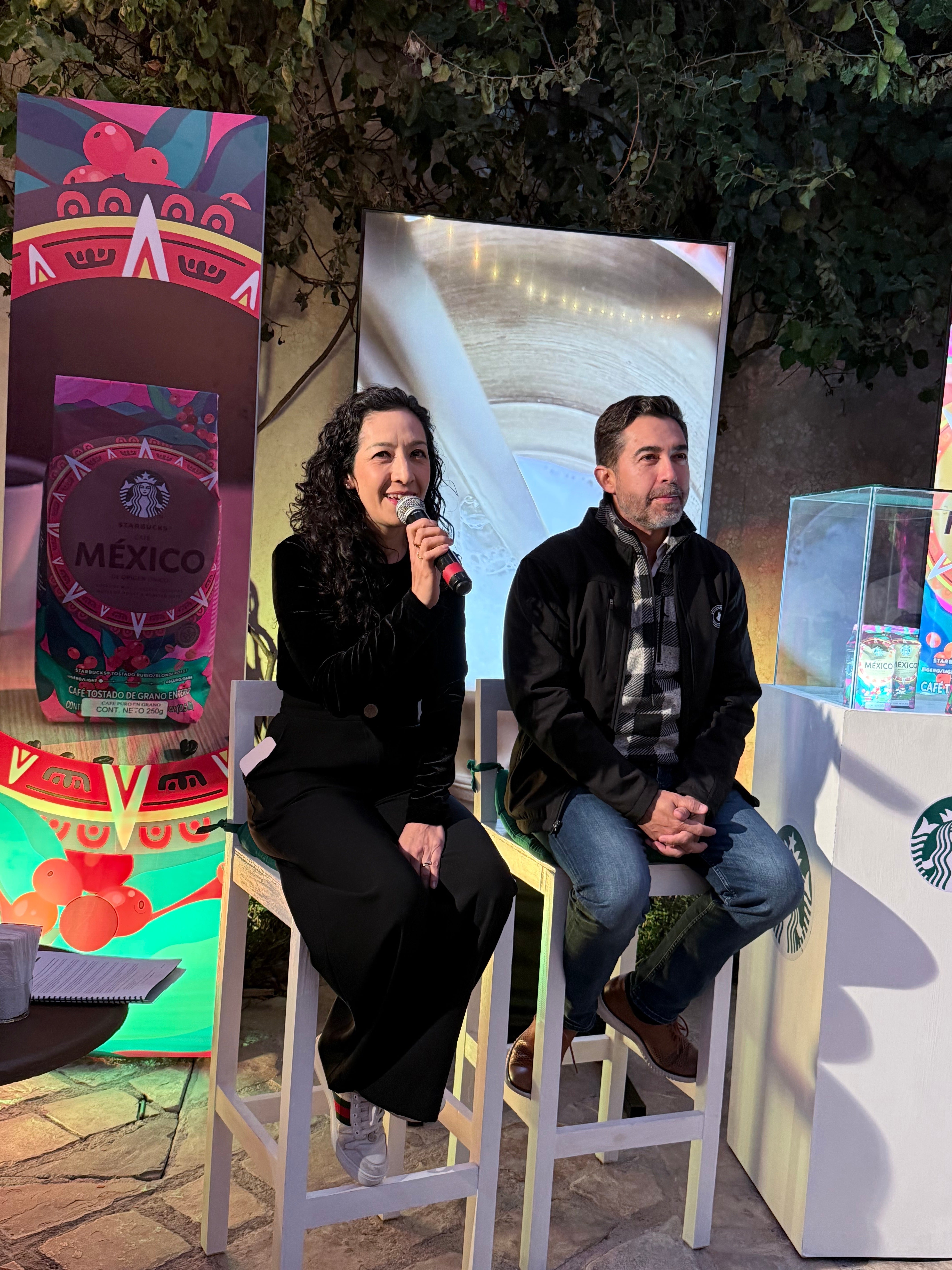 Dos personas sentadas hablando en un evento promocional de Starbucks México, con coloridos paneles de fondo y luces