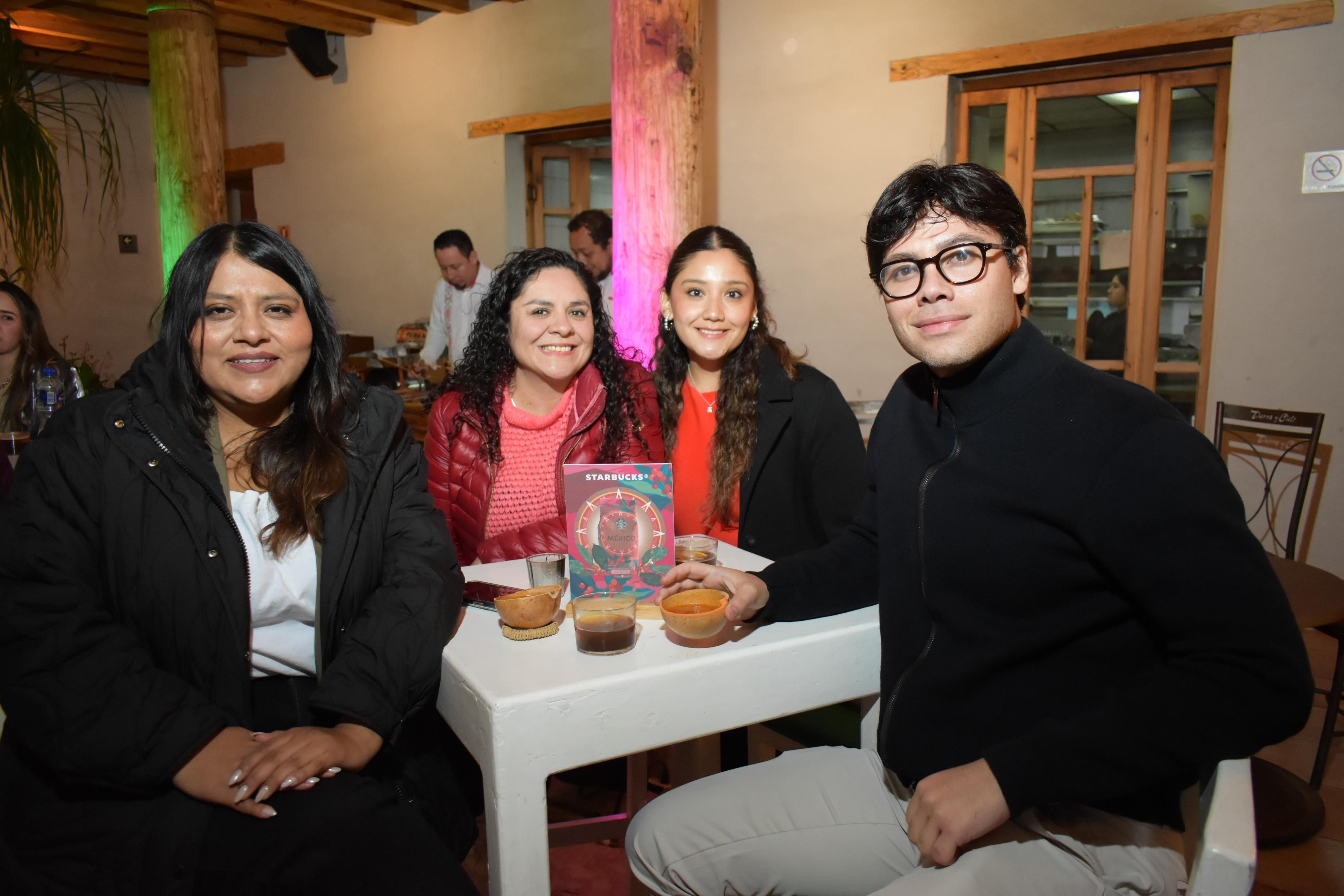 Grupo de cuatro personas sentadas en una mesa con bebidas en un restaurante, sonriendo a la cámara