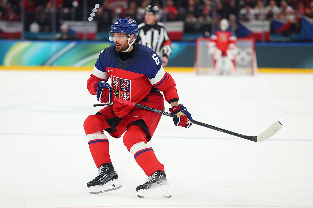 Hockeyspiller i aksjon under en kamp, ​​iført en trøye med et løveemblem, offisiell i bakgrunnen, skøytebane fullpakket med tilskuere