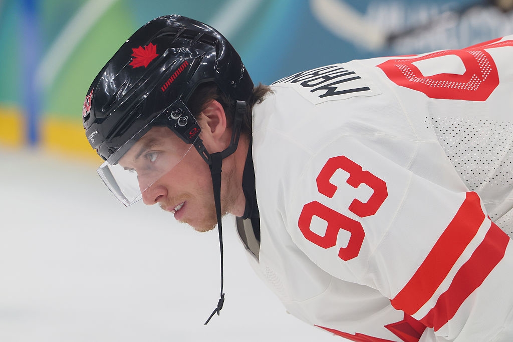 Hockeyspiller iført trøye og hjelm fokuserer intenst under en kamp, ​​kroket i posisjon på isen, klar for action