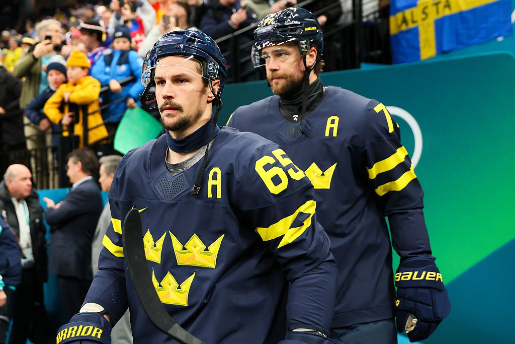 To hockeyspillere iført trøyer med kroner og bokstaven 'A' gå av isen, som representerer Sverige, på en arena med jublende fans