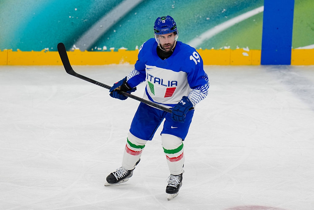 Hockeyspiller som har på seg en "Italia" jersey skøyter på isen med en pinne, fokusert under en kamp
