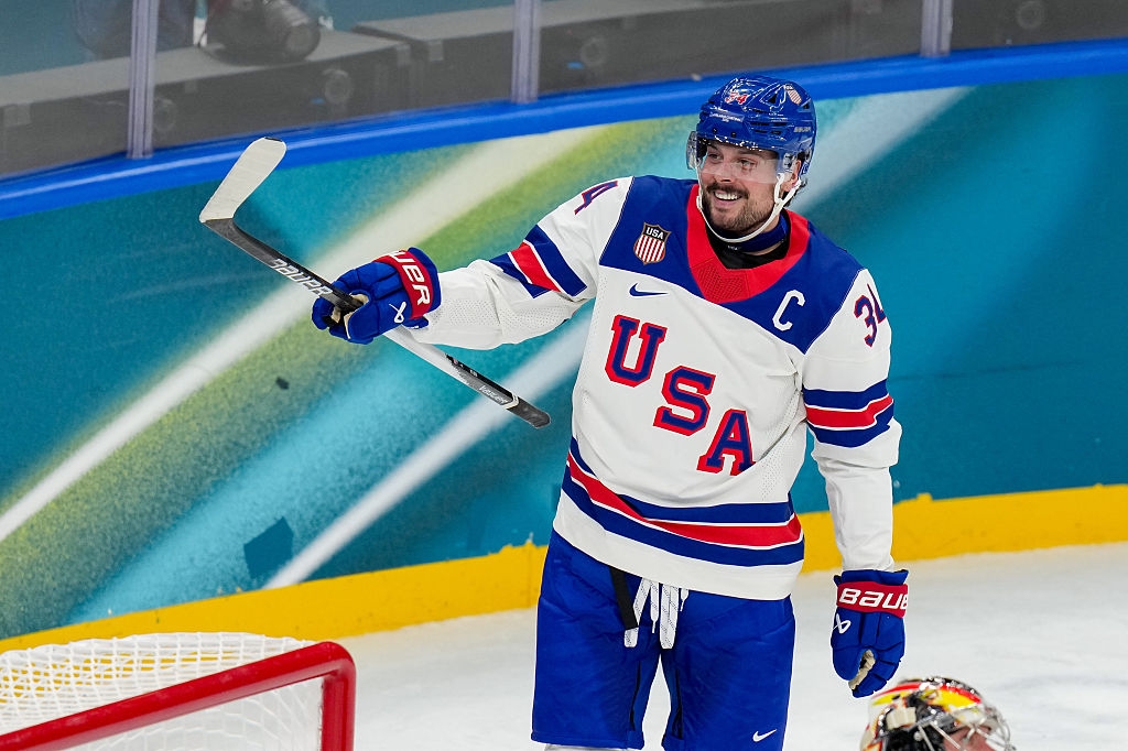 En hockeyspiller iført USA-uniform feirer på isen med en hevet kjepp, iført hjelm og hansker