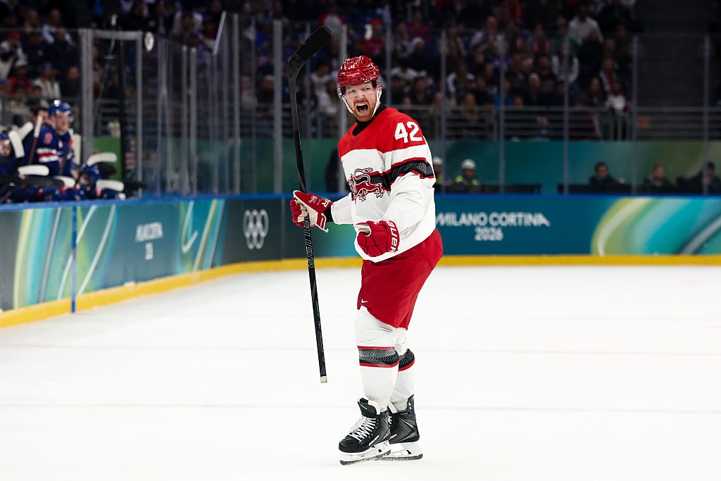 Hockeyspiller feirer på isen under en kamp, ​​iført en laguniform med hjelm og holder en hockeykølle