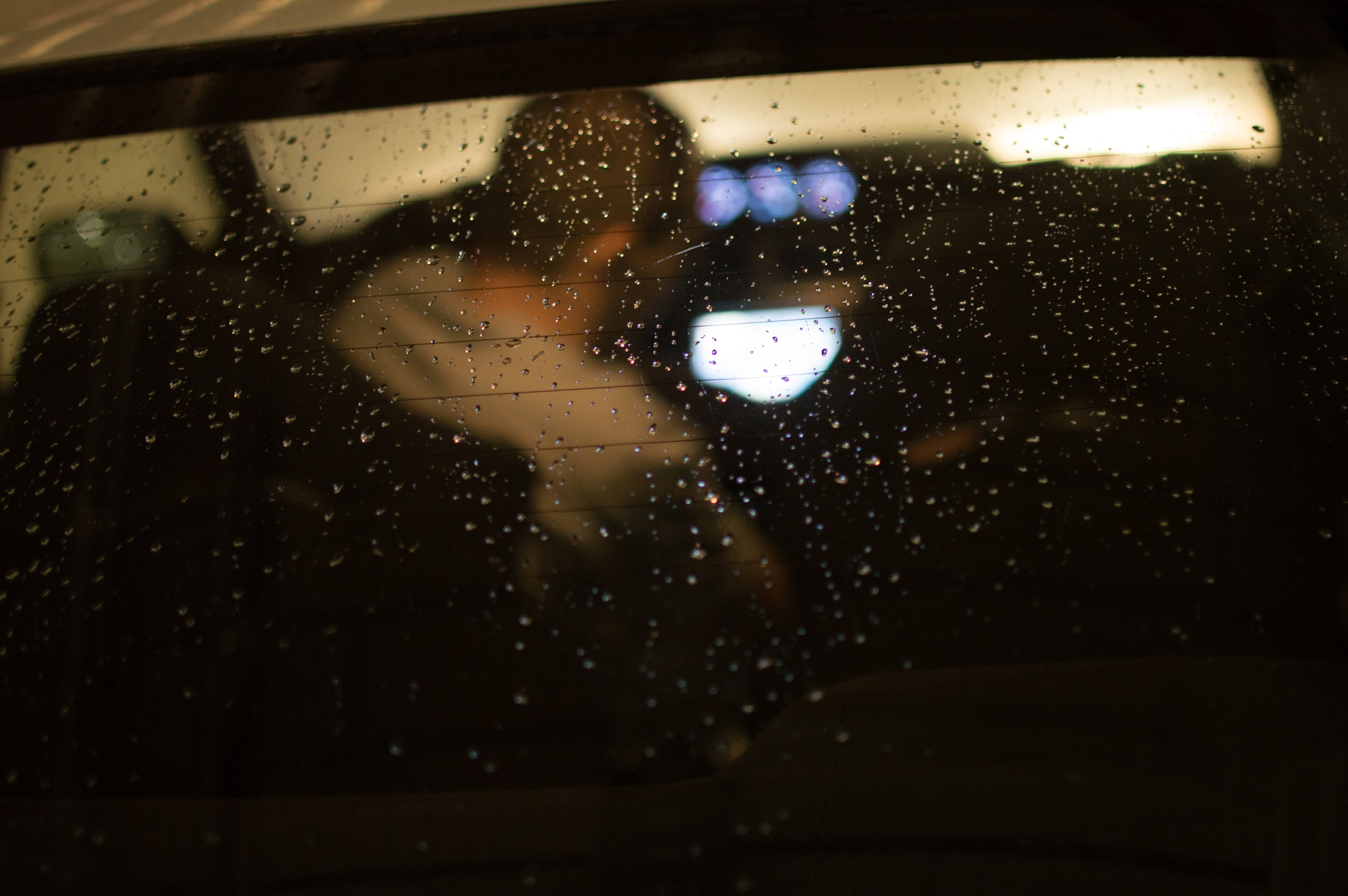 Person seen done  a rain-soaked car   window, focusing connected  illuminated screens wrong  the vehicle