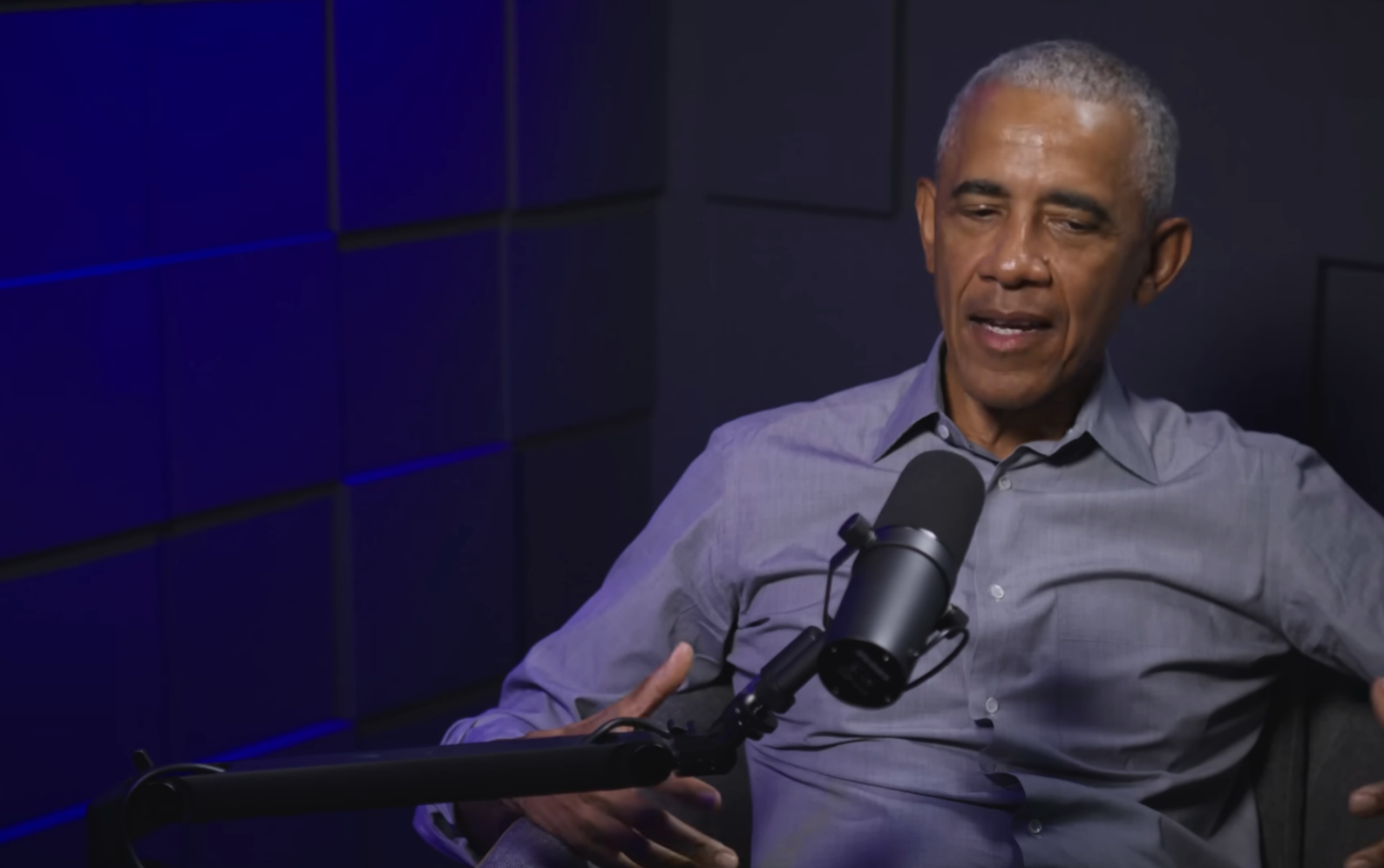 Person speaking into a microphone during a podcast interview. Wearing a casual button-up shirt, sitting successful  a workplace  setting