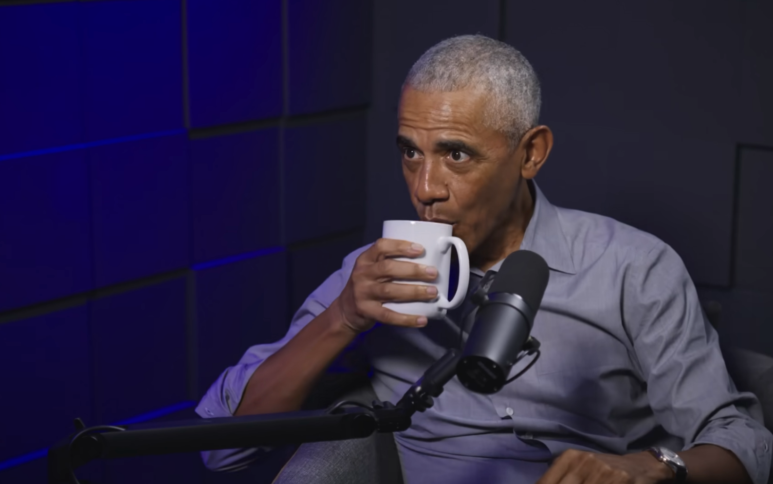 A idiosyncratic   successful  a signaling  workplace  sips from a mug portion    seated astatine  a microphone