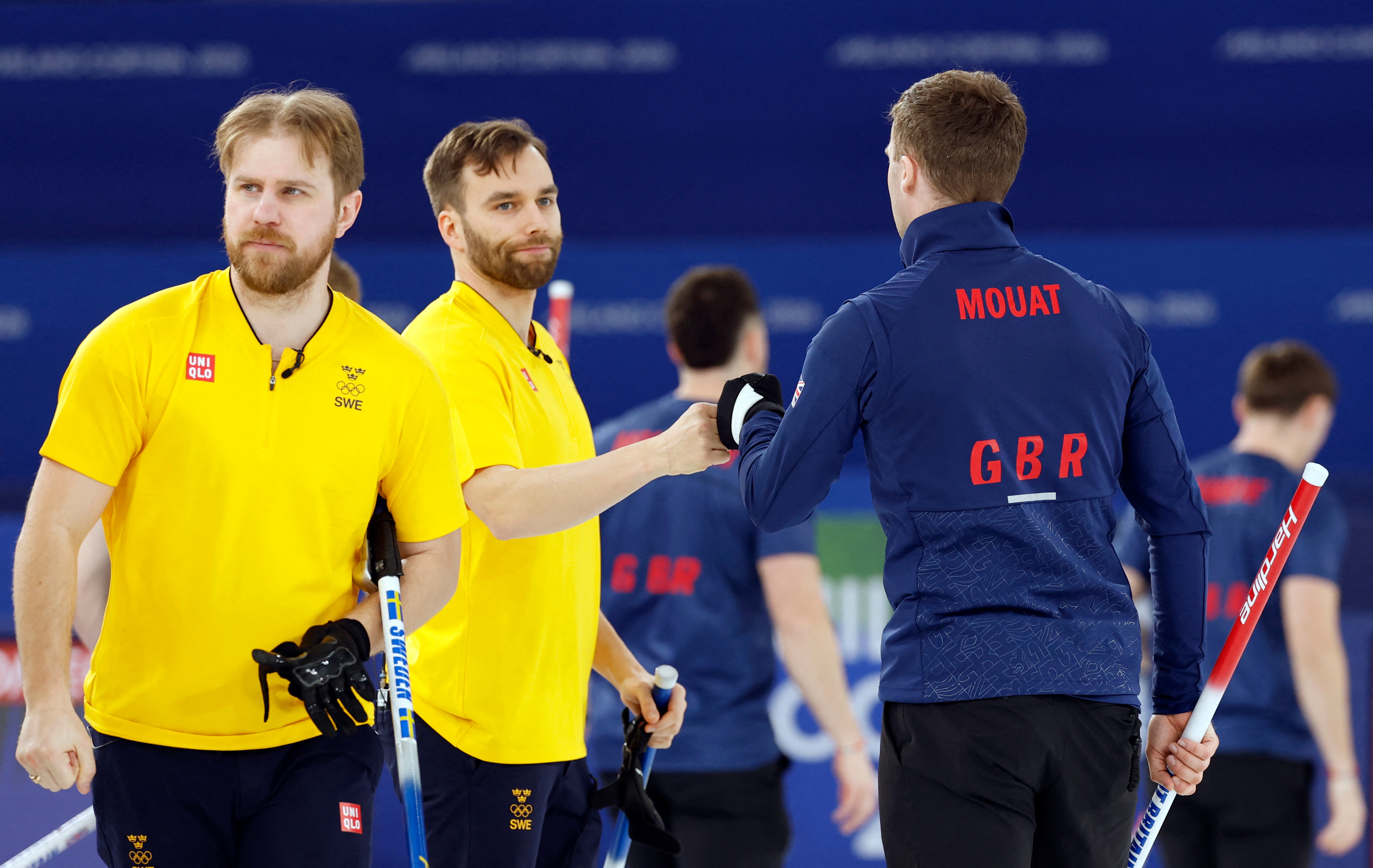 Curling players shingle  hands connected  the ice. Team members deterioration  matching yellowish  and bluish  outfits, portion    the hostile  wears a overgarment   labeled "GBR"