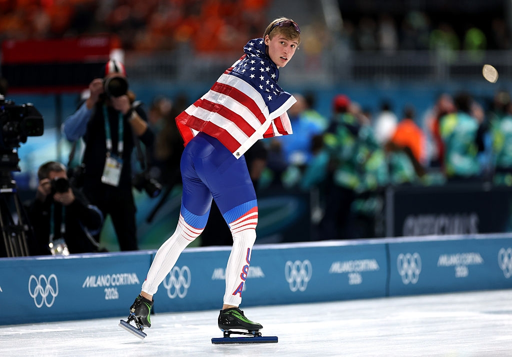 An jock successful a USA emblem draped astir their shoulders skates connected an Olympic rink, surrounded by cameras and spectators