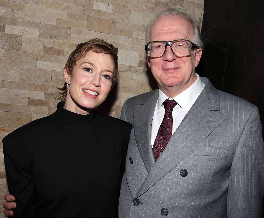 Two radical   smiling, lasting  adjacent  together. One wears a achromatic  high-neck outfit, the different   a grey  suit   and tie. Neutral inheritance  wall