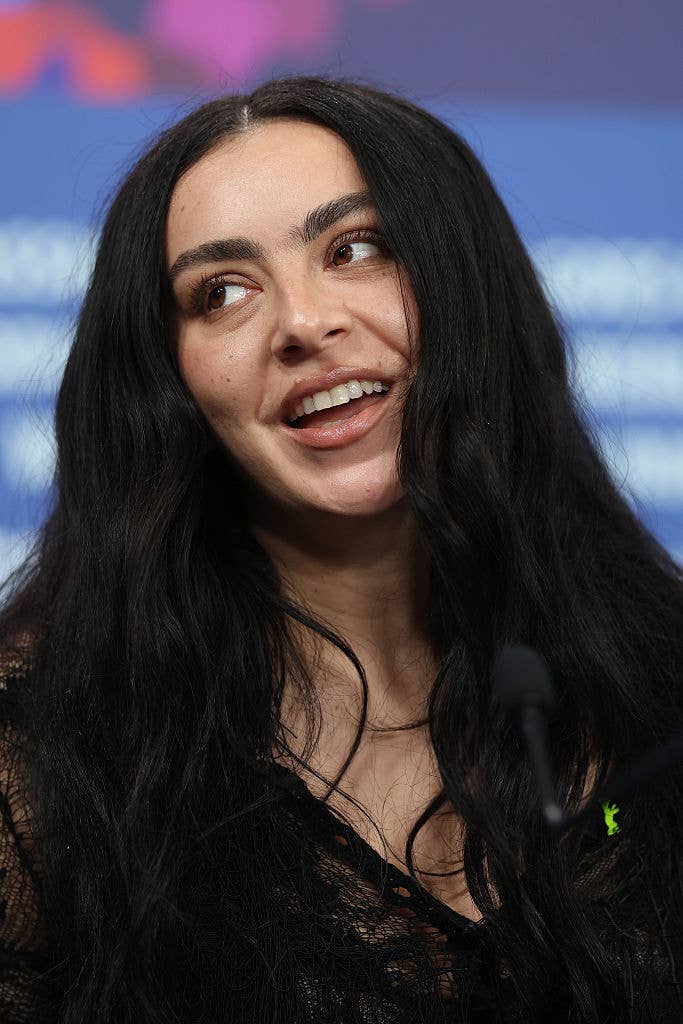 Person with long, acheronian  hairsbreadth  speaking astatine  an event. They are wearing a textured, sheer apical  and look  engaged successful  conversation