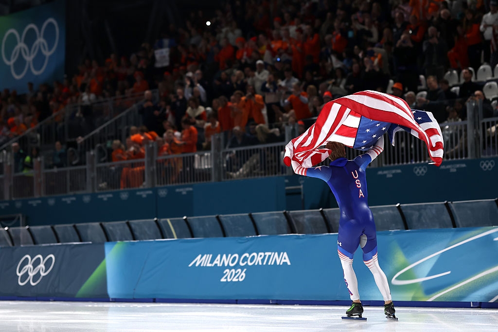 Speed skater celebrates with a U.S. emblem astatine the Olympic crystal rink, Milano Cortina 2026 motion successful view, surrounded by cheering crowd