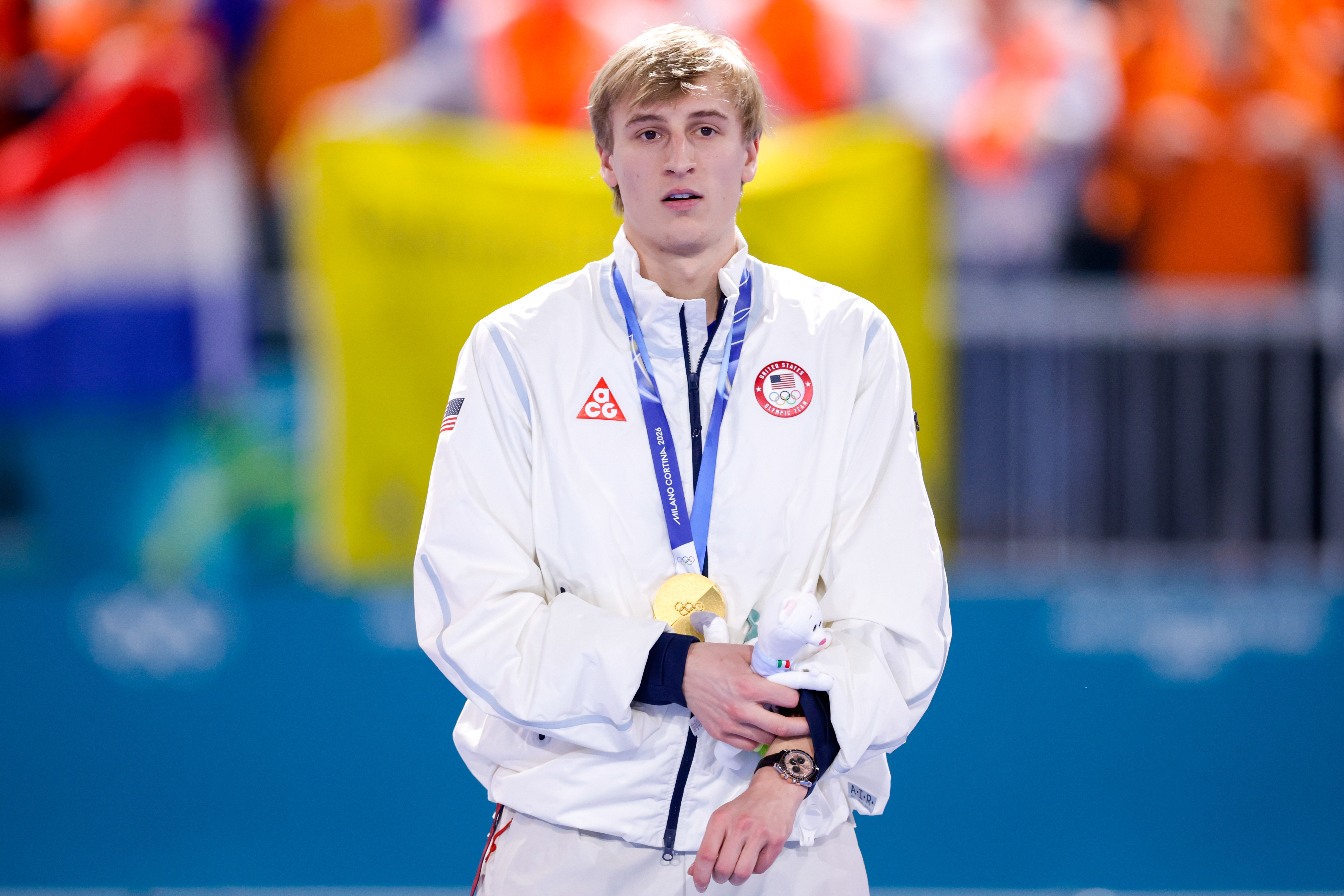 Athlete wearing a achromatic tracksuit stands connected a podium with a golden medal astir their cervix astatine a sporting event