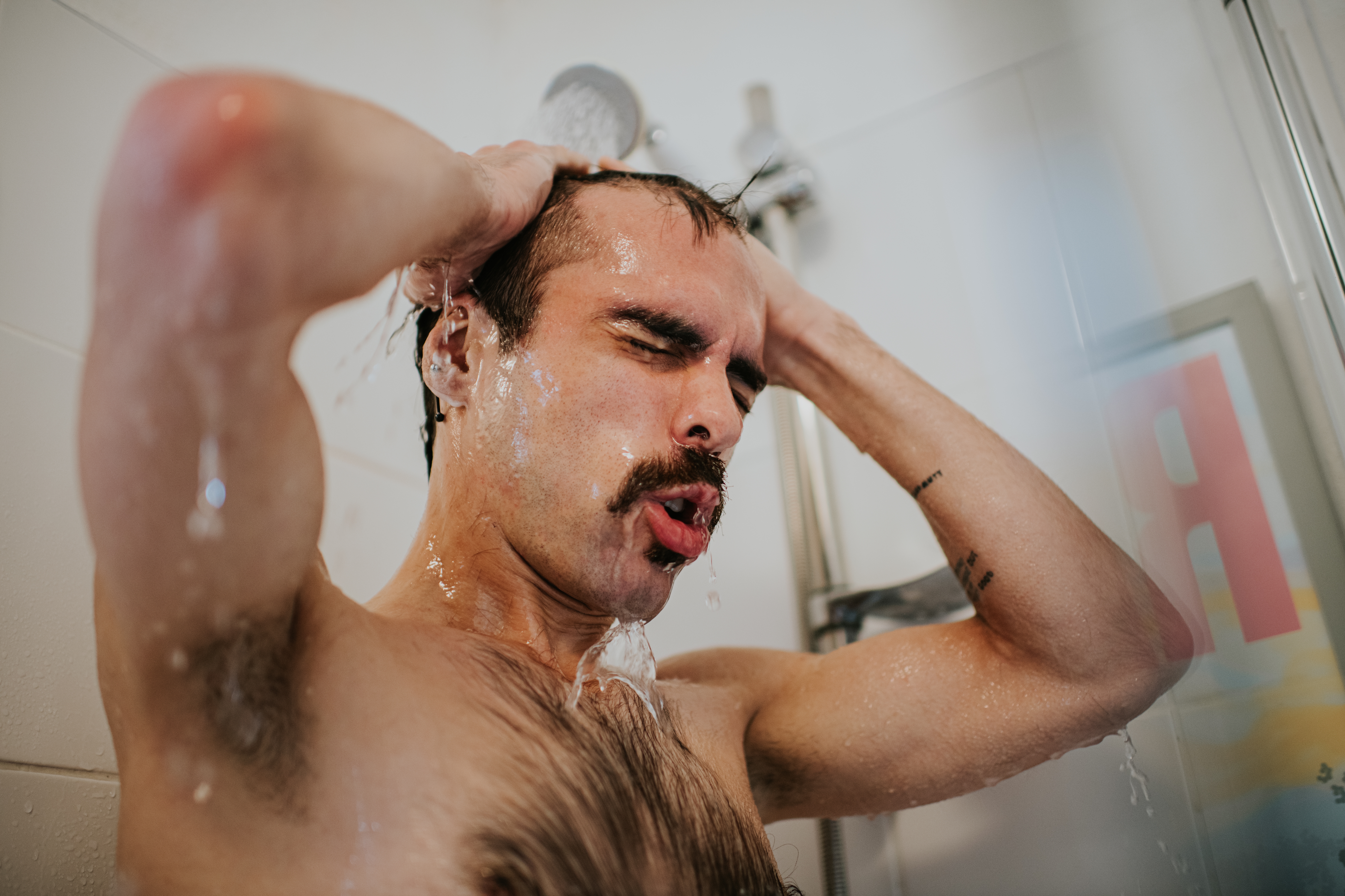 Person with a mustache showering, eyes closed, hands in hair, conveying a sense of relaxation and pleasure