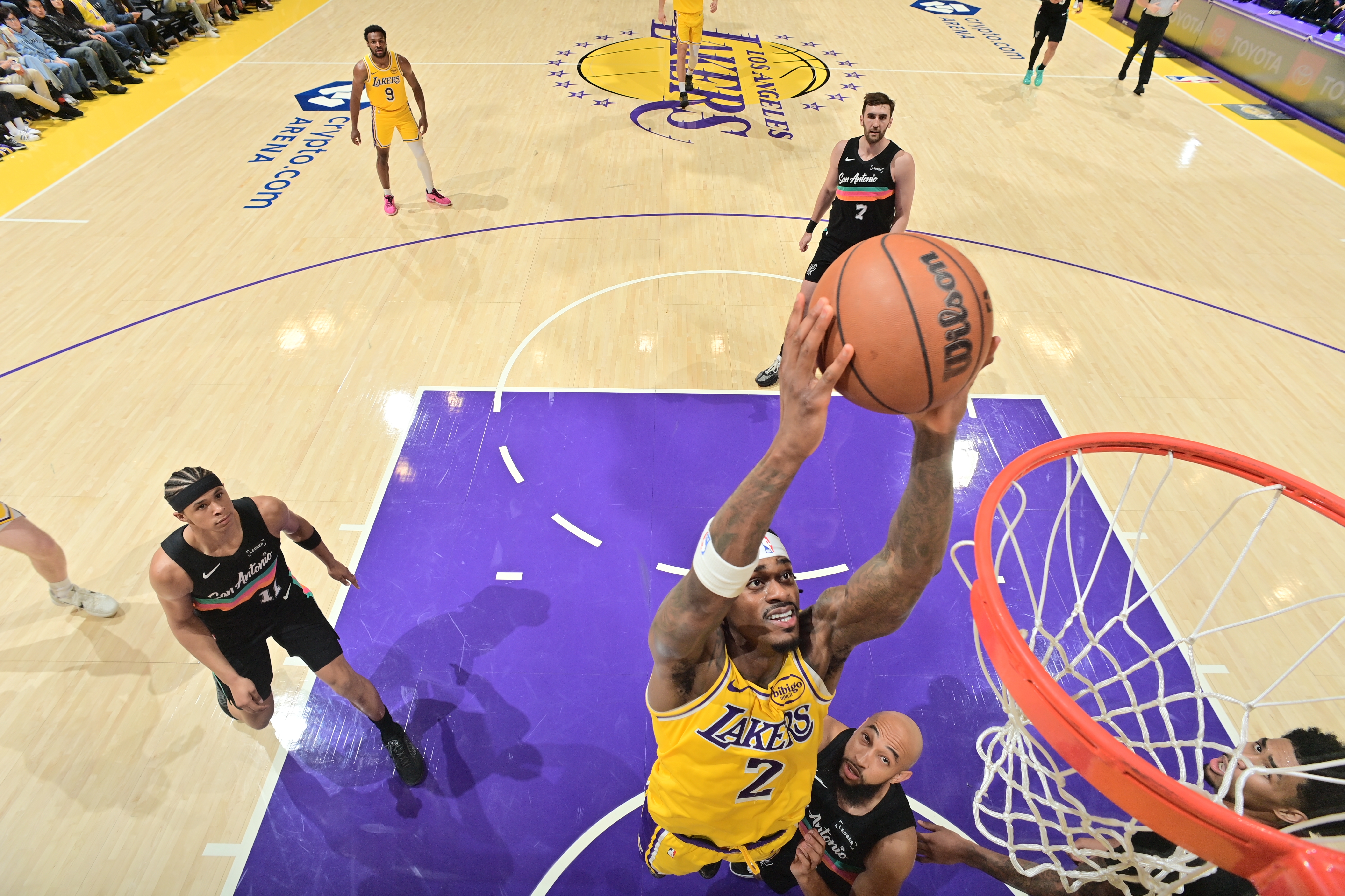 Basketball subordinate    successful  a Lakers jersey performs a slam dunk during a game, with opponents looking connected  from below