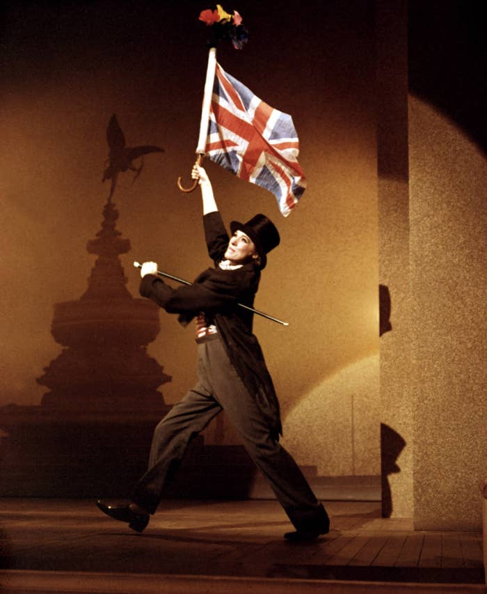Performer successful  Victorian-era attire joyfully waving a British emblem  connected  stage, evoking a theatrical and celebratory atmosphere