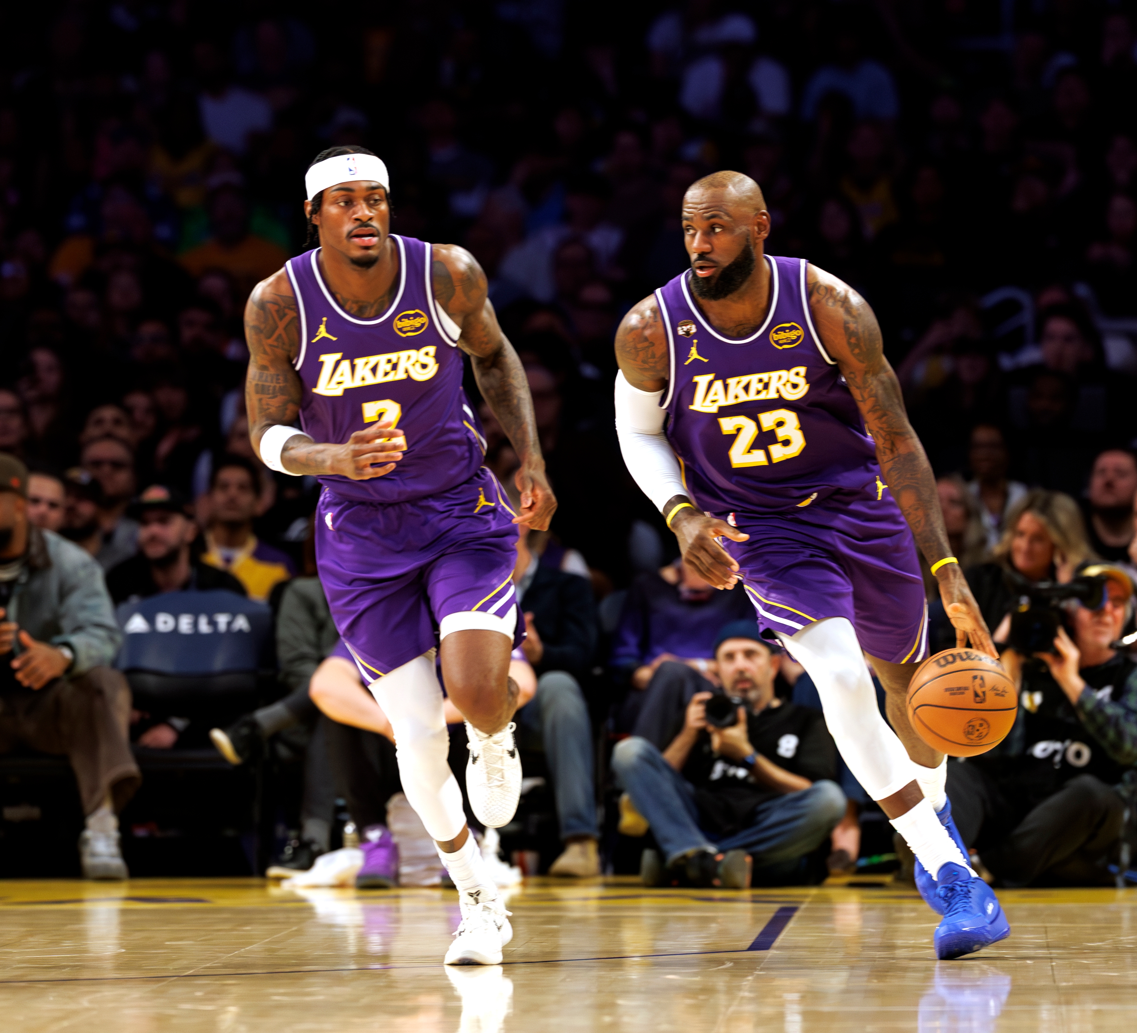 Two hoops  players successful  enactment   during a game, wearing Lakers uniforms. One dribbles the ball, portion    the different   runs alongside