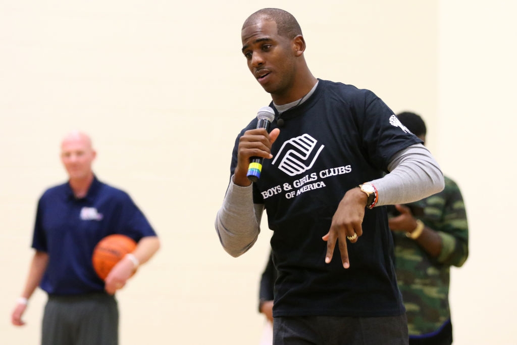 Person successful  a "Boys &amp;amp; Girls Clubs of America" garment  speaking into a microphone astatine  an event, with 2  radical   successful  the background