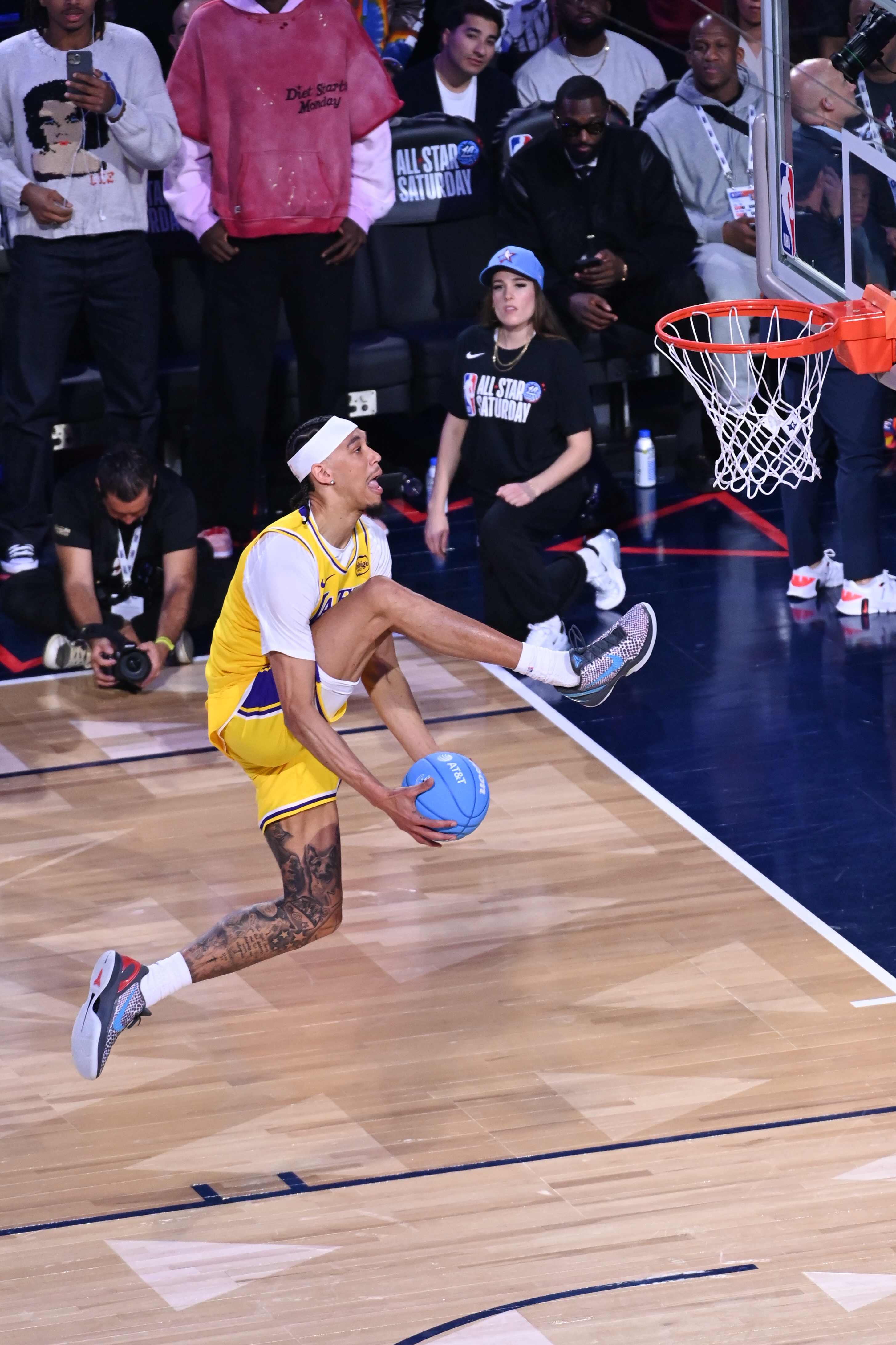 Basketball subordinate    mid-air, holding bluish  ball, astir  to dunk during a crippled  event. Crowd and photographers ticker  intently