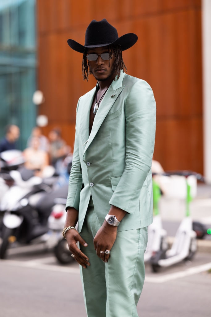 Person successful  stylish suit   with a cowboy chapeau  and sunglasses connected  an municipality  street