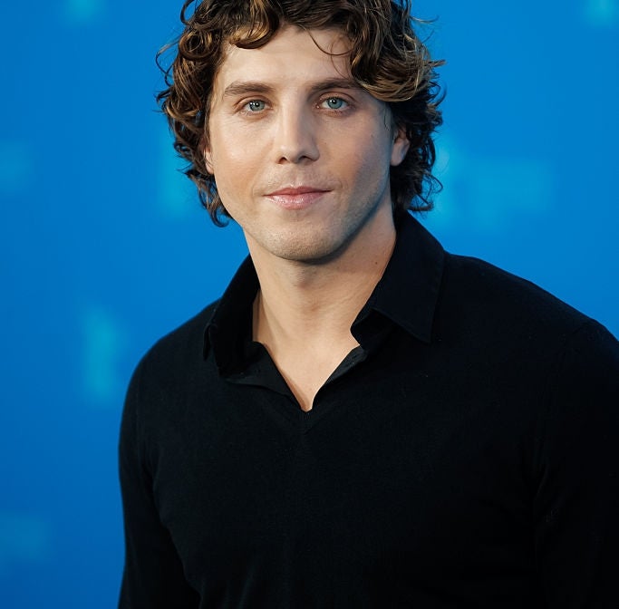Person with curly hairsbreadth  successful  a achromatic  garment  stands against a plain backdrop, looking astatine  the camera