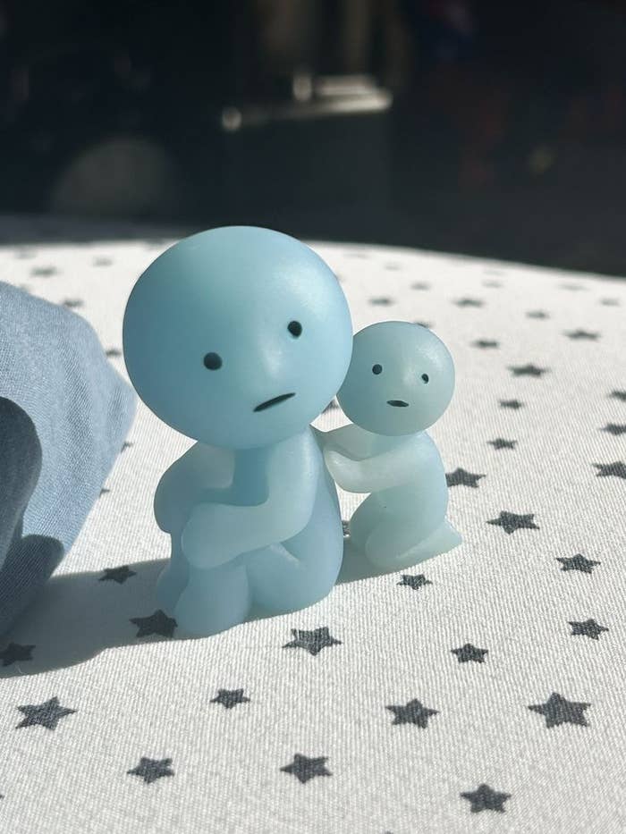 Dos figuras pequeñas de estilo minimalista con expresiones neutrales sobre una tela con estampado de estrellas