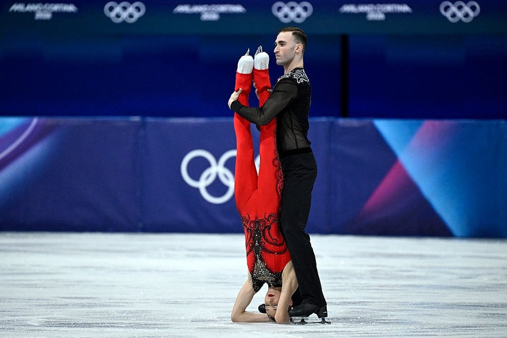 Figure skating pair performs an impressive head-over-heels lift on the ice during a competition, displaying athleticism and elegance
