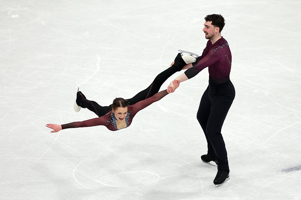 To skøyteløpere utfører et løft, med mannen som holder kvinnen horisontalt med en arm og et ben under en rutine på skøytebanen